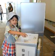 4歳くらいの女の子が投票箱に投票している様子